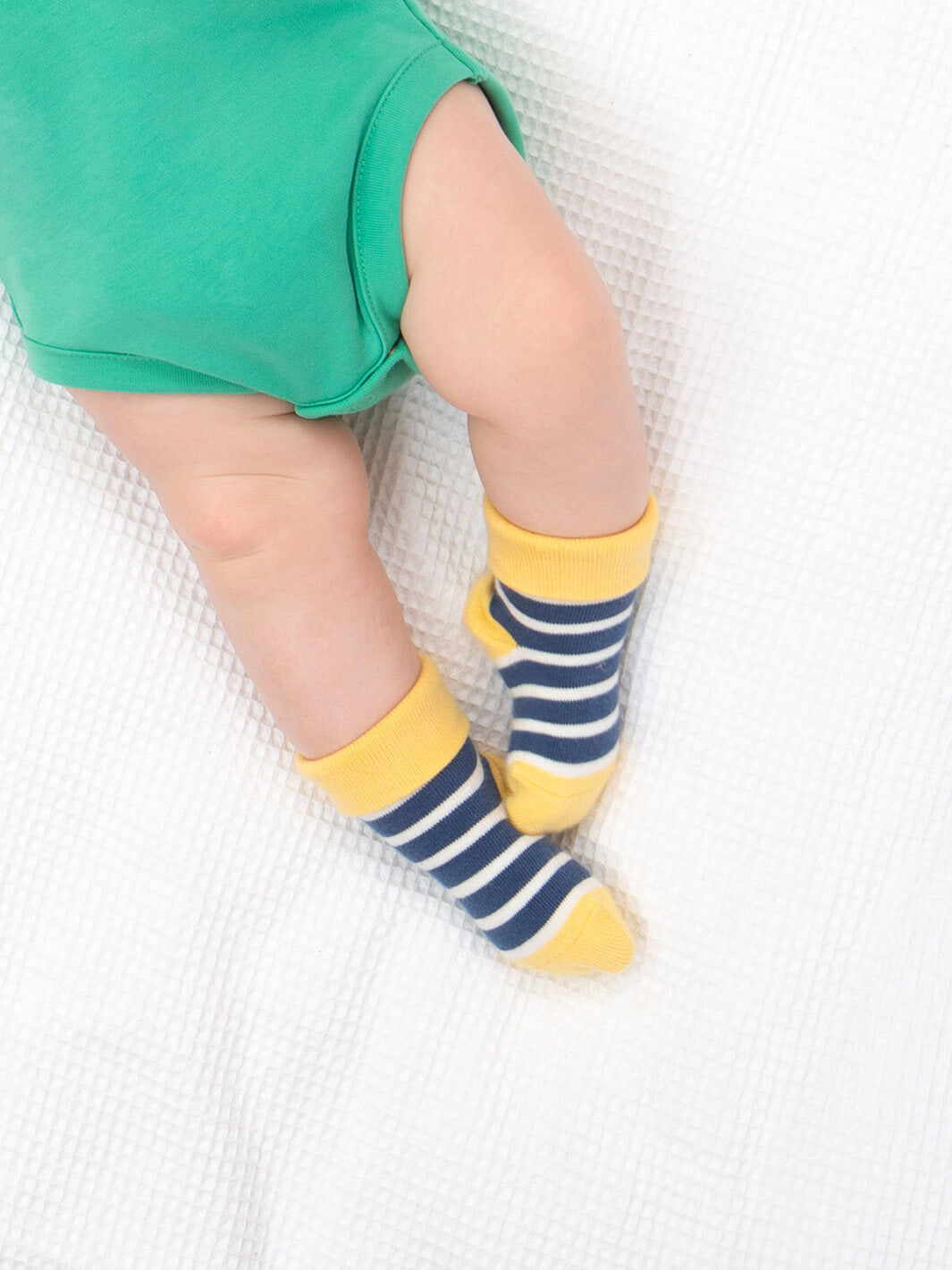 Bebé usando calcetines de rayas azul marino y amarillo de algodón orgánico, parte del pack arcoíris.