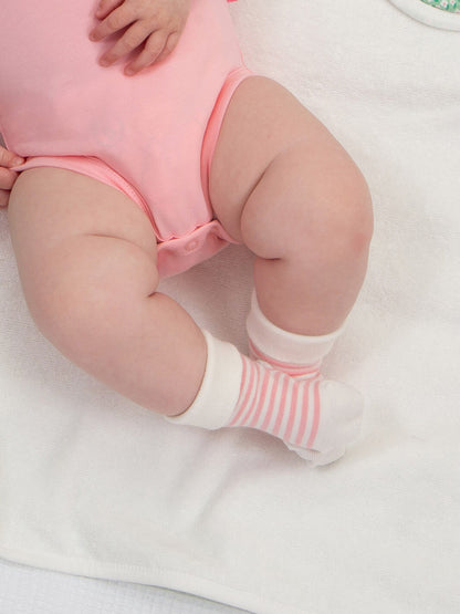 Bebé usando calcetines de rayas rosadas y blancas de algodón orgánico, modelo Flores Fantásticas.