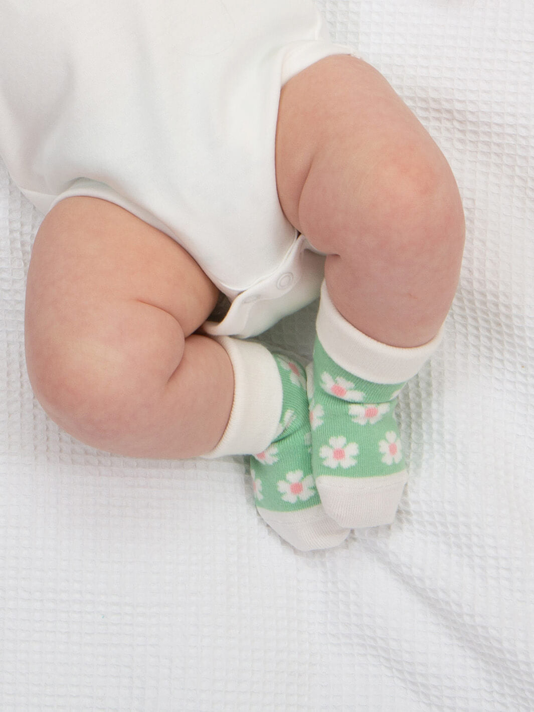 Bebé usando calcetines verdes con flores blancas y rosas, pack Flores Fantásticas