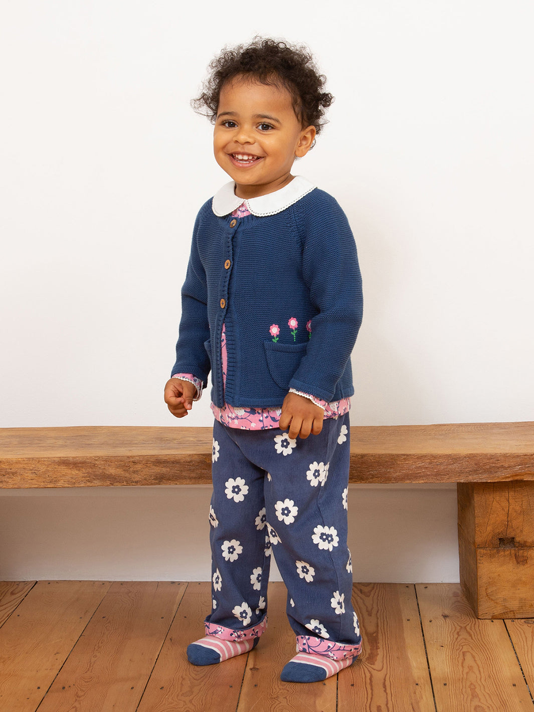 Niña vistiendo el Chaleco Floral de algodón orgánico, combinado con calzas para un look cómodo y tierno.