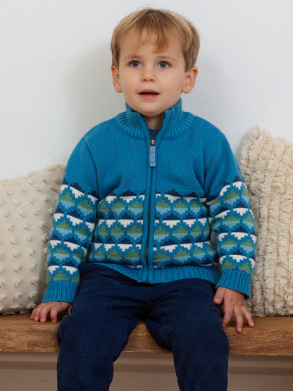 Niño usando chaqueta Nido azul clásico de algodón orgánico con diseño geométrico de triángulos verdes y blancos, abrigo de invierno infantil.