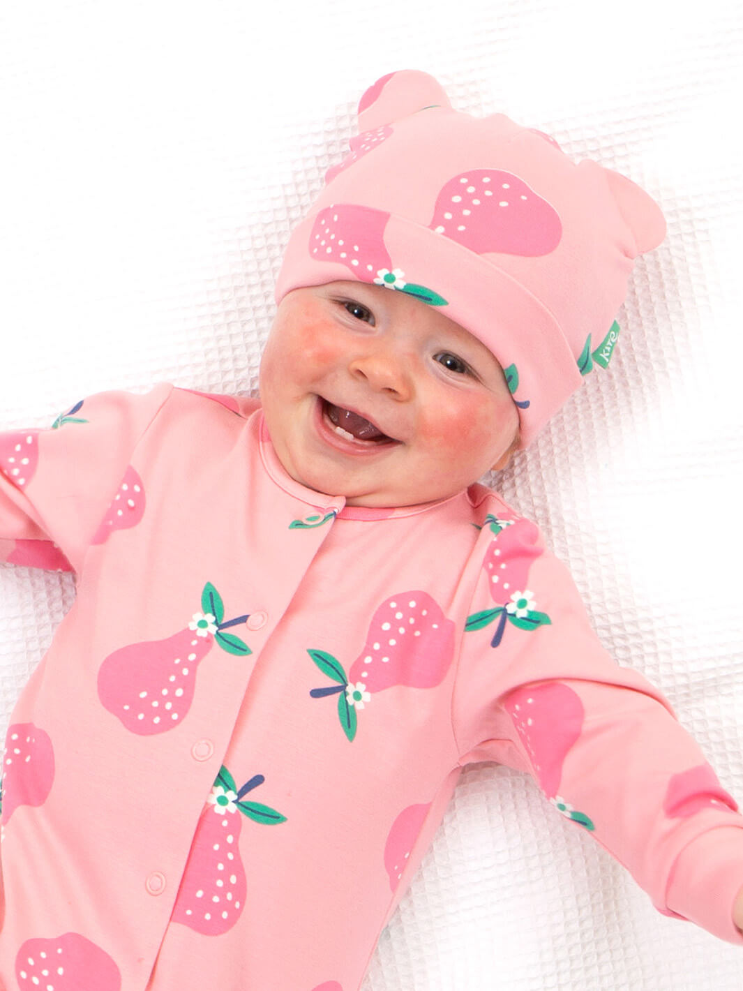 Bebé usando gorro rosa de algodón orgánico con peras y orejitas a juego con enterito estampado
