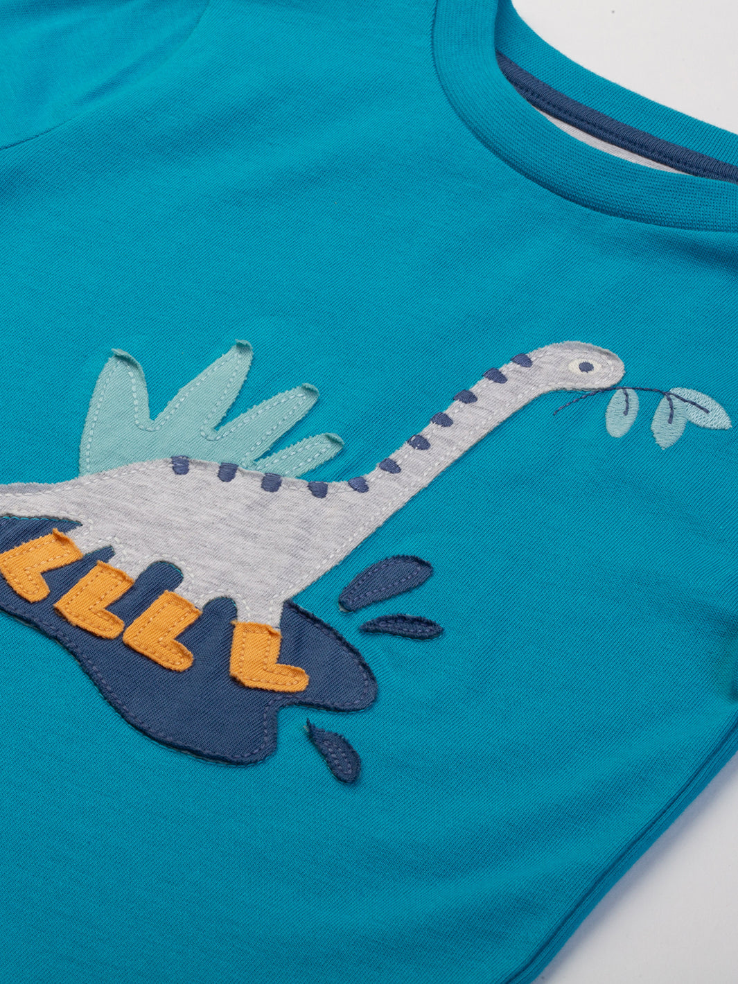 Detalle del aplique de dinosaurio en la Polera Dino Feliz de algodón orgánico, diseño divertido y certificado OEKO-TEX.