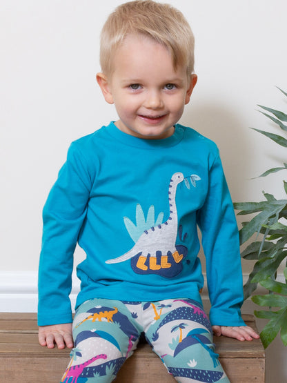 Niño usando la Polera Dino Feliz de algodón orgánico, combinada con calzas de dinosaurios para un look divertido y aventurero.
