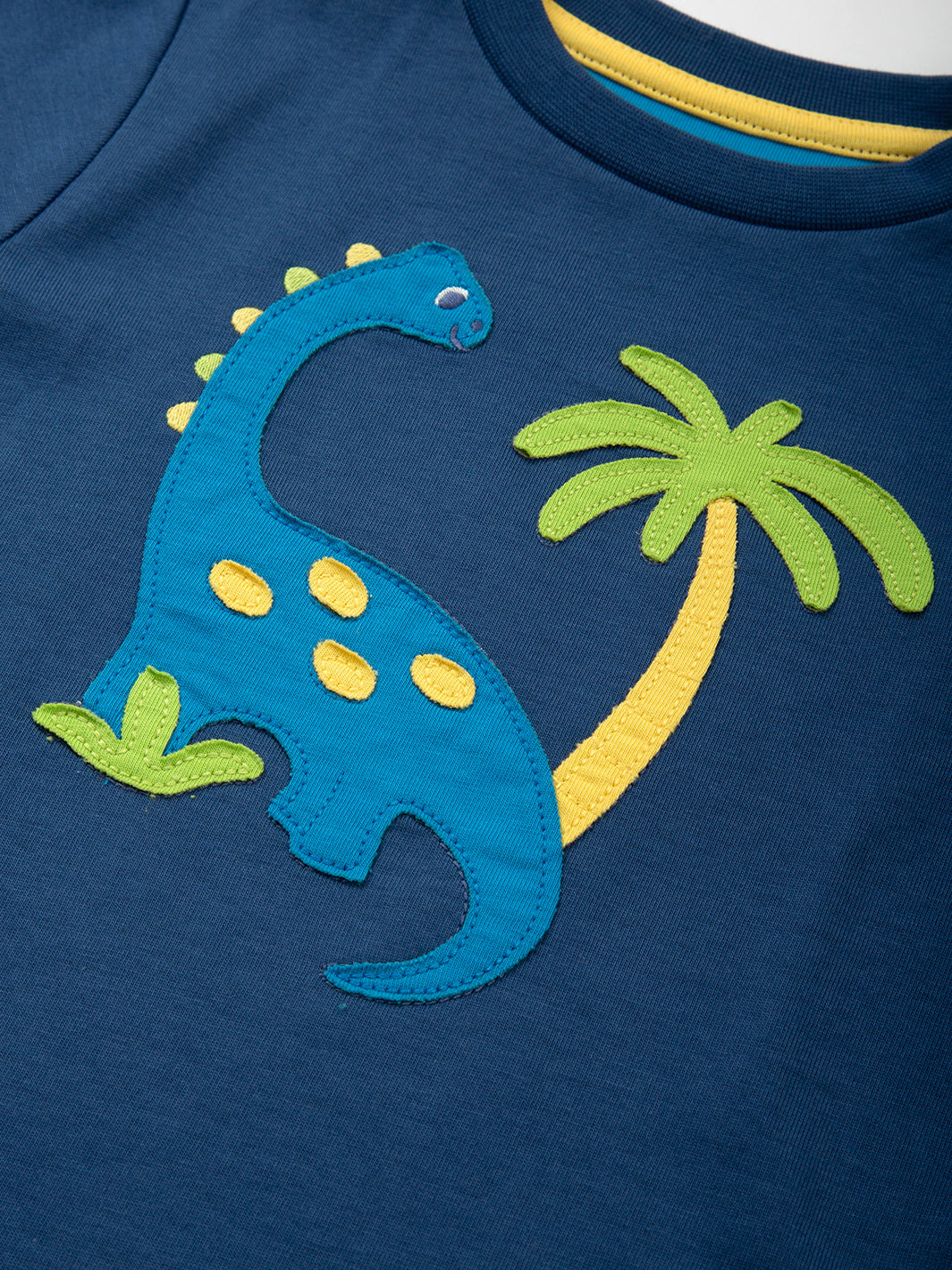 Detalle del aplique de dinosaurio en la Polera Tierra de Dinosaurios de algodón orgánico, diseño divertido y certificado OEKO-TEX.