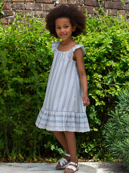 Niña vistiendo el Vestido Haven de algodón orgánico con rayas azul marino y crema, luciendo su diseño fresco con volantes y bordado en el dobladillo.